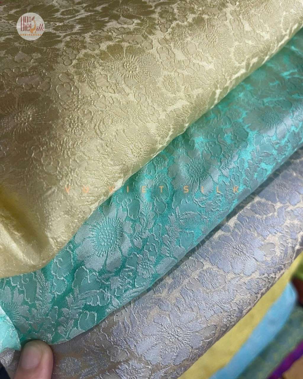 Bốn dòng sản phẩm lụa tơ tằm Nha Xá được bày cạnh nhau trên nền vải lanh tự nhiên: cuộn vải lụa nguyên liệu màu hồng phấn, chiếc khăn lụa gấp hình hoa hồng màu xanh ngọc, bao gối lụa trắng ngà, và chiếc cà vạt lụa xanh đen. Mỗi sản phẩm kèm tag nhỏ ghi 